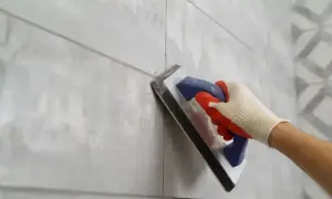 Ręka w rękawicy nakłada fugę żywiczną na szare płytki.