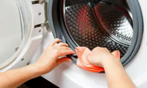 Ręce czyszczą uszczelkę pralki pomarańczową ściereczką. Dowiedz się, czym wyczyścić pralkę, by służyła latami.