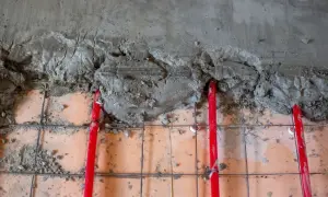 Budowa podłogi z ogrzewaniem: czerwone rury grzewcze, siatka zbrojeniowa i świeży cement. Różne rodzaje cementu mogą być używane do takich prac.