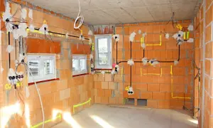 Rozpoczyna się instalacja elektryczna w domu. Widoczne przewody, puszki i oznaczenia na ścianach z cegły.