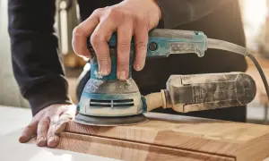 Ręce majsterkowicza wykonują szlifowanie drewna za pomocą szlifierki. Powierzchnia deski staje się gładka.