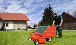 Ogrodnik wykonuje wertykulację trawnika za pomocą pomarańczowego urządzenia.