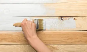 Ręka maluje białą farbą drewnianą boazerię. Proces odnawiania wnętrza trwa.