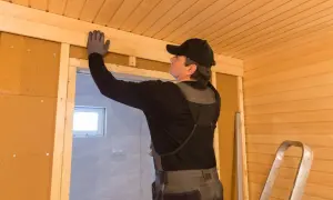 Budowa sauny w domu. Mężczyzna w rękawiczkach montuje drewniane wykończenie sufitu.