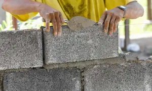 Budowniczy układa bloczki betonowe fundamentowe, nakładając zaprawę kielnią. Solidne fundamenty to podstawa każdej budowy.