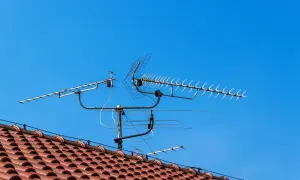 Na dachu domu, pod błękitnym niebem, zamontowana jest wieloelementowa antena TV.