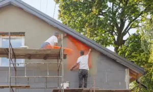 Pracownicy na rusztowaniach montują siatkę elewacyjną, przygotowując budynek do termomodernizacji.