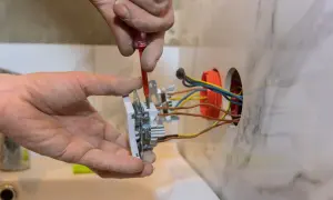 Instalator przykręca gniazdko, pokazując, jak podłączyć gniazdko. Widać przewody i puszkę instalacyjną.