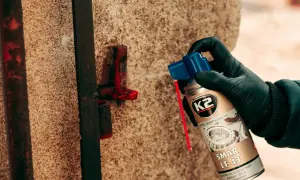 Ręka w czarnej rękawiczce aplikuje smar K2 LT-43 na zardzewiały element bramy.