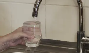 Ręka trzyma szklankę pod strumieniem wody z kranu.