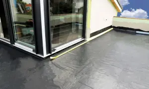 Nowoczesna hydroizolacja na balkon z czarnej membrany, chroniąca przed wilgocią. Widoczny fragment budynku i okna.
