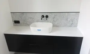 Nowoczesna łazienka z czarnymi szafkami, białą umywalką i blatem z konglomeratu.