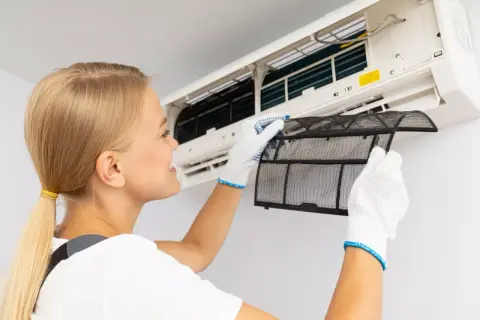 Kobieta w białych rękawiczkach wyjmuje filtr z klimatyzacji domowej. Dba o czyste powietrze.