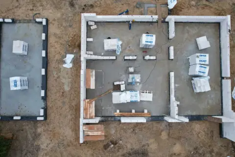 Budowa domu z bloczków betonowych. Materiały budowlane leżą na płycie fundamentowej, czekając na montaż ścian, by zapewnić niski współczynnik przenikania ciepła.