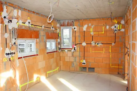 Rozpoczyna się instalacja elektryczna w domu. Widoczne przewody, puszki i oznaczenia na ścianach z cegły.