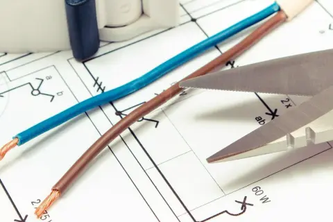 Niebieski i brązowy kabel leżą na schemacie elektrycznym. Czy czerwony kabel to plus czy minus? Nożyczki zbliżają się do przewodów.