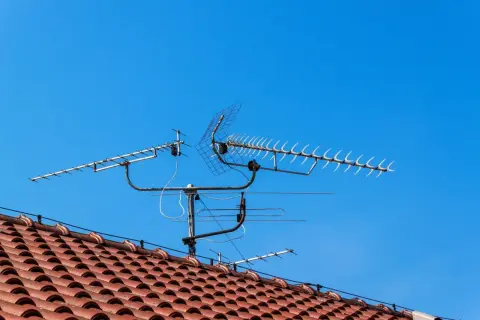 Na dachu domu, pod błękitnym niebem, zamontowana jest wieloelementowa antena TV.