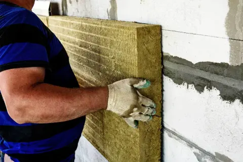 Pracownik montuje wełnę mineralną na ścianie. Ocieplenie wełną cena robocizny jest kluczowa dla budżetu.