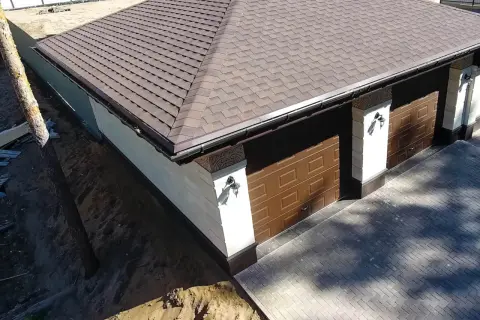 Nowy dach z gontu pokrywa budynek z dwoma brązowymi bramami garażowymi.