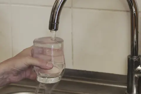 Ręka trzyma szklankę pod strumieniem wody z kranu.