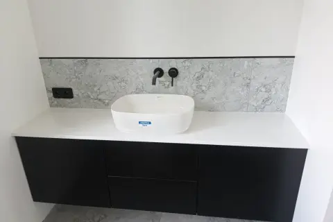 Nowoczesna łazienka z czarnymi szafkami, białą umywalką i blatem z konglomeratu.