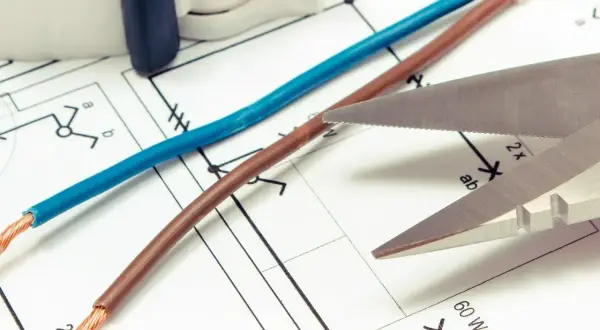 Niebieski i brązowy kabel leżą na schemacie elektrycznym. Czy czerwony kabel to plus czy minus? Nożyczki zbliżają się do przewodów.