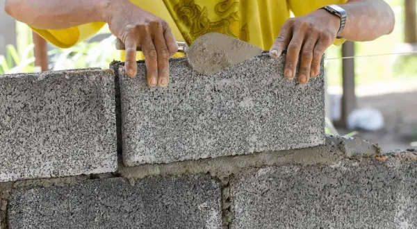 Budowniczy układa bloczki betonowe fundamentowe, nakładając zaprawę kielnią. Solidne fundamenty to podstawa każdej budowy.