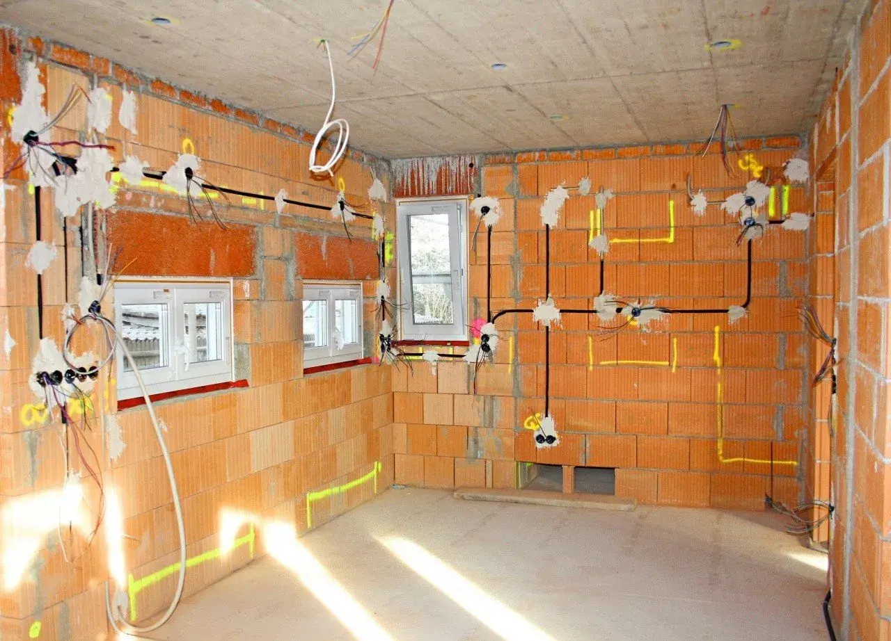 Rozpoczyna się instalacja elektryczna w domu. Widoczne przewody, puszki i oznaczenia na ścianach z cegły.