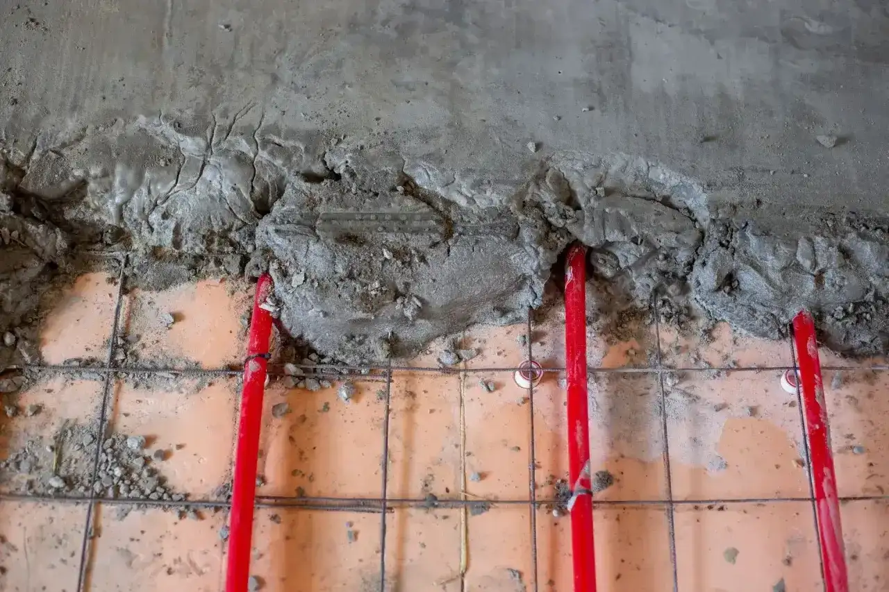 Budowa podłogi z ogrzewaniem: czerwone rury grzewcze, siatka zbrojeniowa i świeży cement. Różne rodzaje cementu mogą być używane do takich prac.