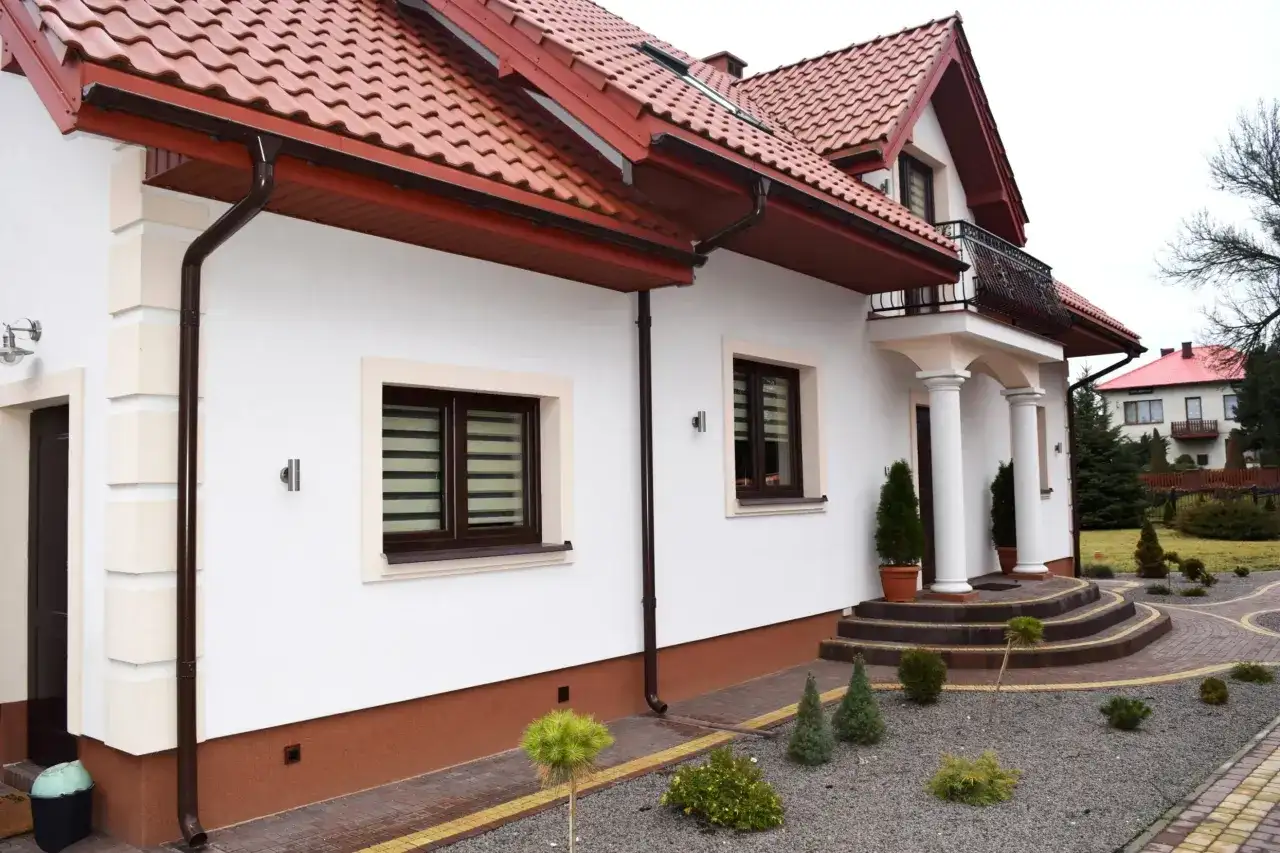 Elegancki dom z białymi ścianami i brązowym cokołem. Podkreśla to, z czego zrobić cokół wokół domu, aby uzyskać taki efekt.