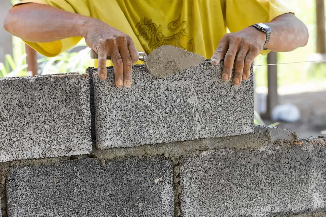 Budowniczy układa bloczki betonowe fundamentowe, nakładając zaprawę kielnią. Solidne fundamenty to podstawa każdej budowy.