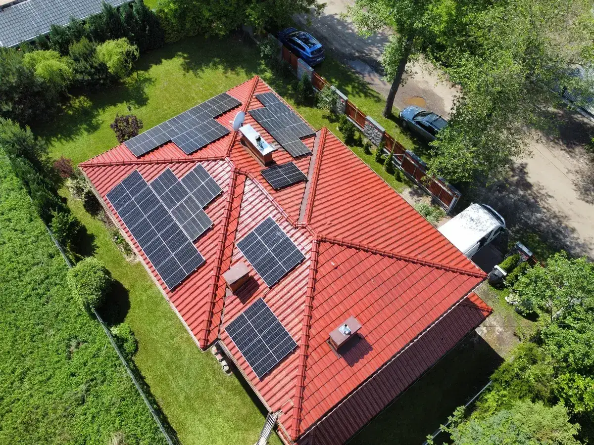 Nowoczesna instalacja fotowoltaiczna na czerwonym dachu domu jednorodzinnego. Panele słoneczne zbierają energię, zapewniając ekologiczne zasilanie.