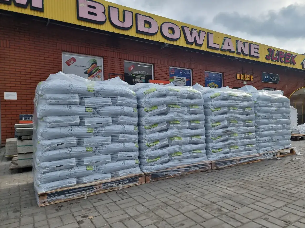 Duże stosy worków z materiałami budowlanymi przed sklepem. Sprawdź aktualną eko groszek cenę!