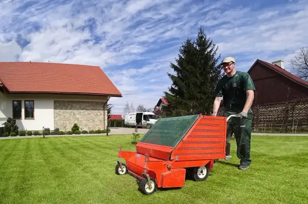 Ogrodnik wykonuje wertykulację trawnika za pomocą pomarańczowego urządzenia.