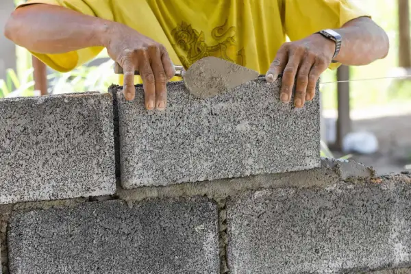 Budowniczy układa bloczki betonowe fundamentowe, nakładając zaprawę kielnią. Solidne fundamenty to podstawa każdej budowy.