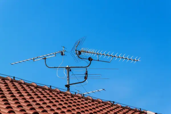 Na dachu domu, pod błękitnym niebem, zamontowana jest wieloelementowa antena TV.