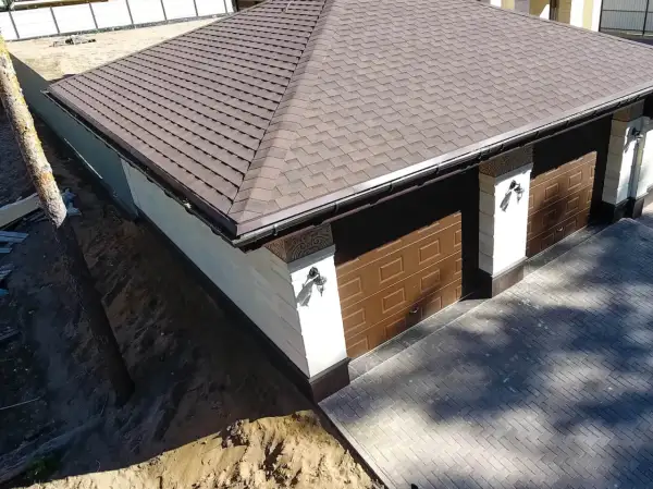 Nowy dach z gontu pokrywa budynek z dwoma brązowymi bramami garażowymi.