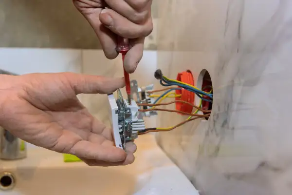Instalator przykręca gniazdko, pokazując, jak podłączyć gniazdko. Widać przewody i puszkę instalacyjną.