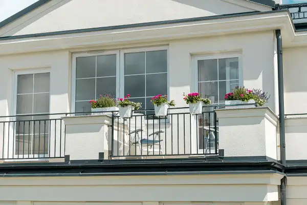 Białe okna pięknie komponują się z jasną, kremową elewacją budynku. Balkon ozdobiony kwiatami dodaje uroku.