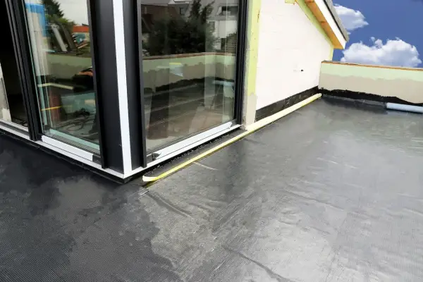 Nowoczesna hydroizolacja na balkon z czarnej membrany, chroniąca przed wilgocią. Widoczny fragment budynku i okna.