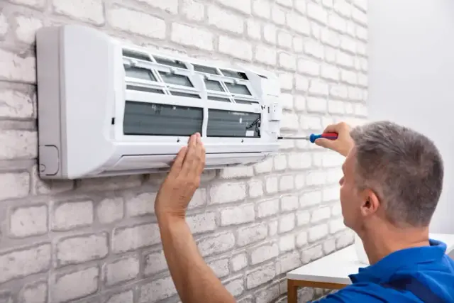 Serwisant montuje klimatyzację bez jednostki zewnętrznej. Wkręca śrubę w białe urządzenie na ceglanej ścianie.
